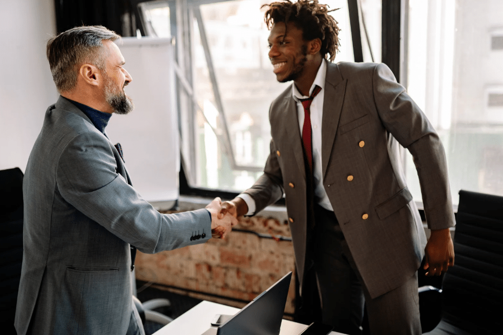 Photo of two men shaking hands and smiling at each other